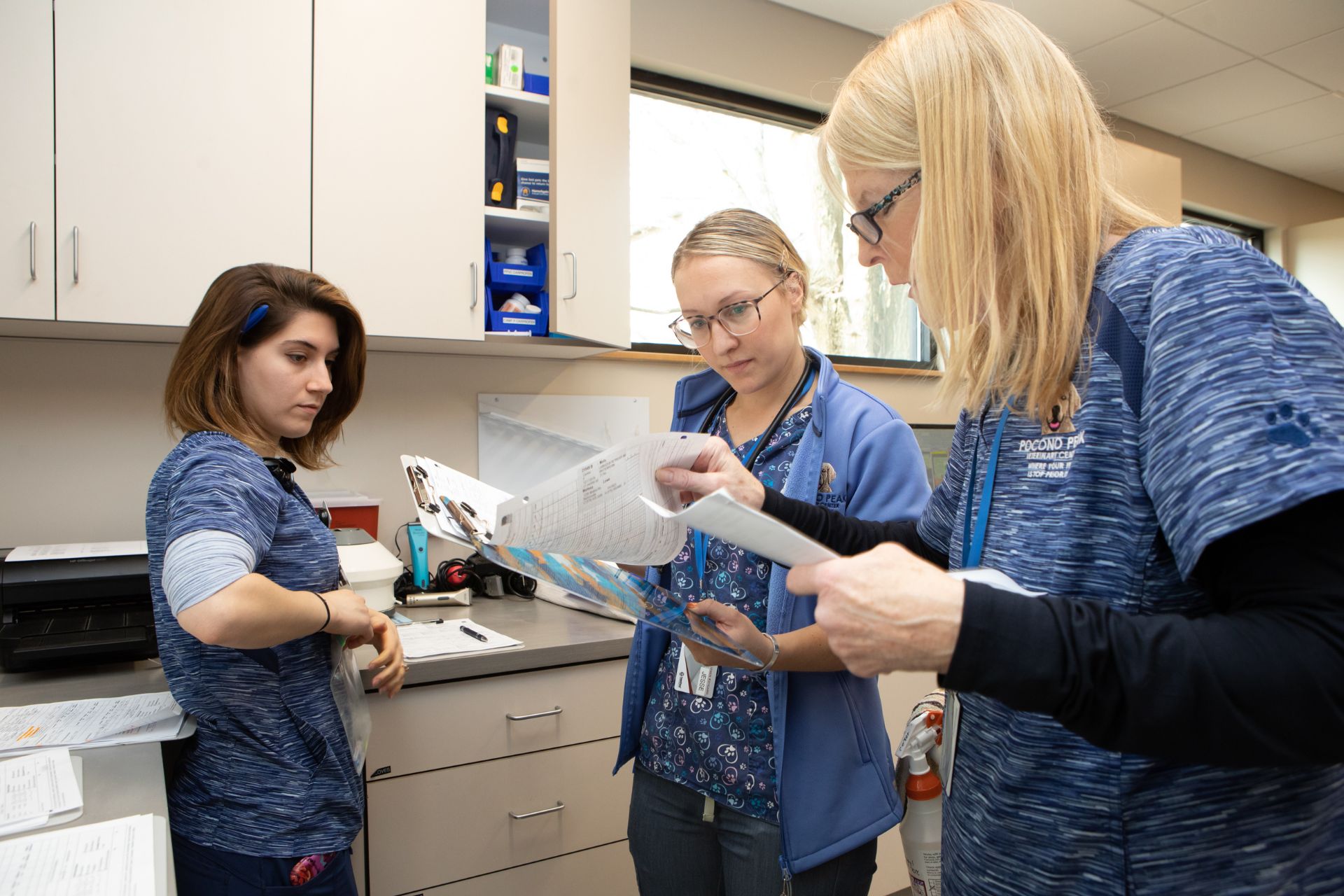 three women in scrubs are looking at a piece of paper