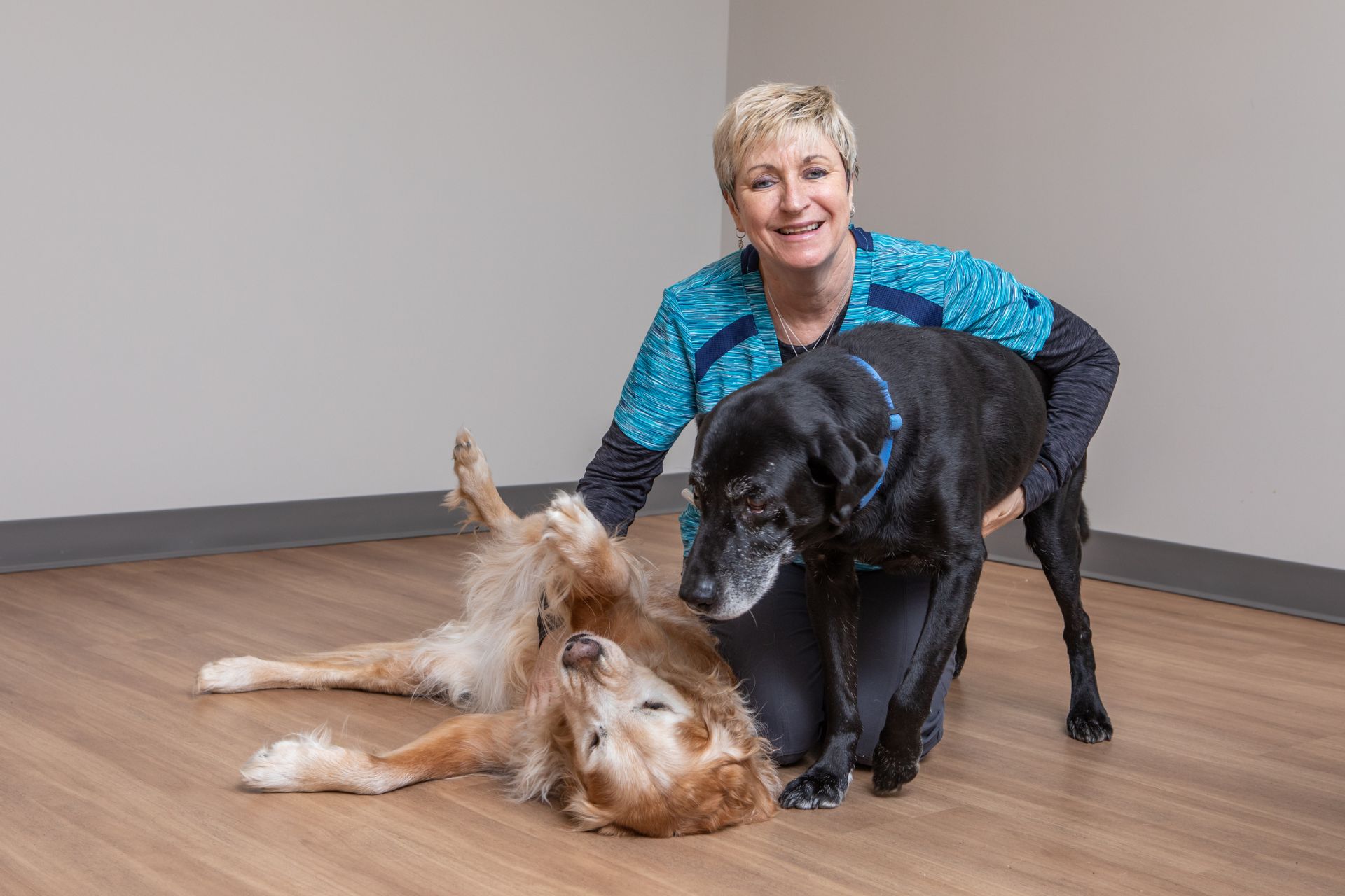 a woman kneeling down with two dogs on the floor